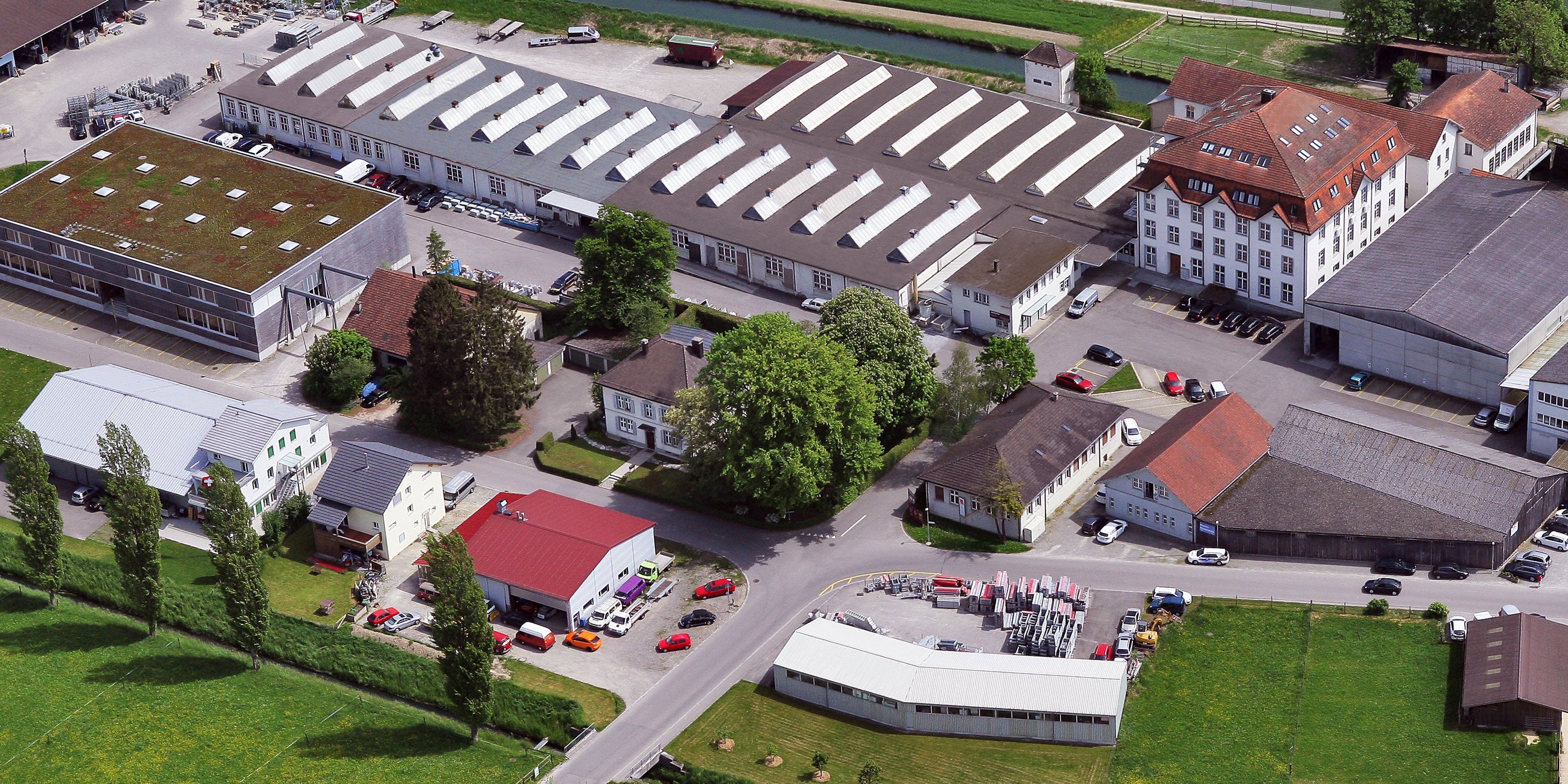Luftaufnahme des VSP-Areals mit Gebäuden, Produktionshallen, Parkplätzen, Autos, Wiesen und Bäumen.