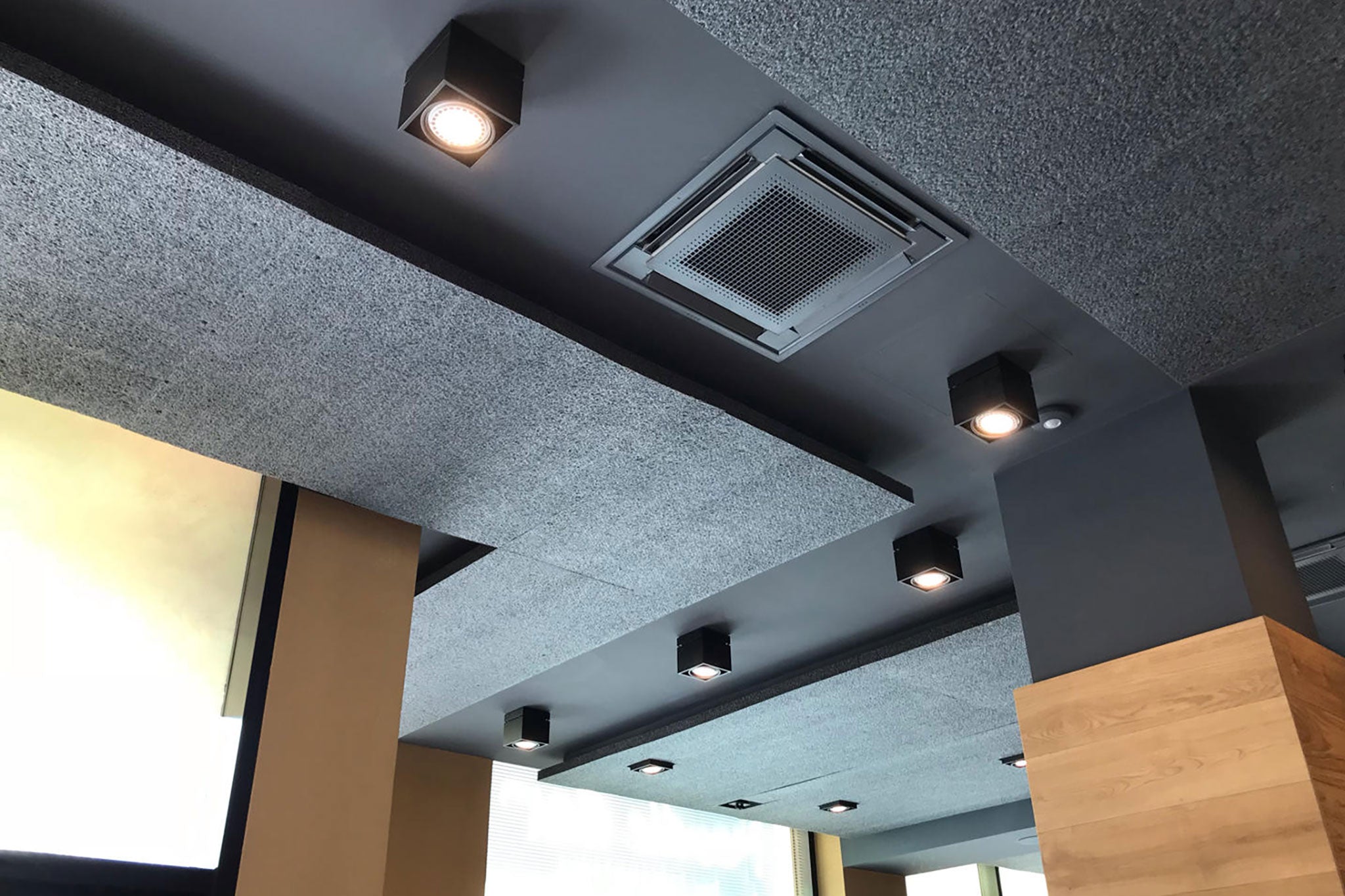 Restaurant mit schwarzer Decke, Holzsäulen und schwarzen Schallabsorbern an der Decke.